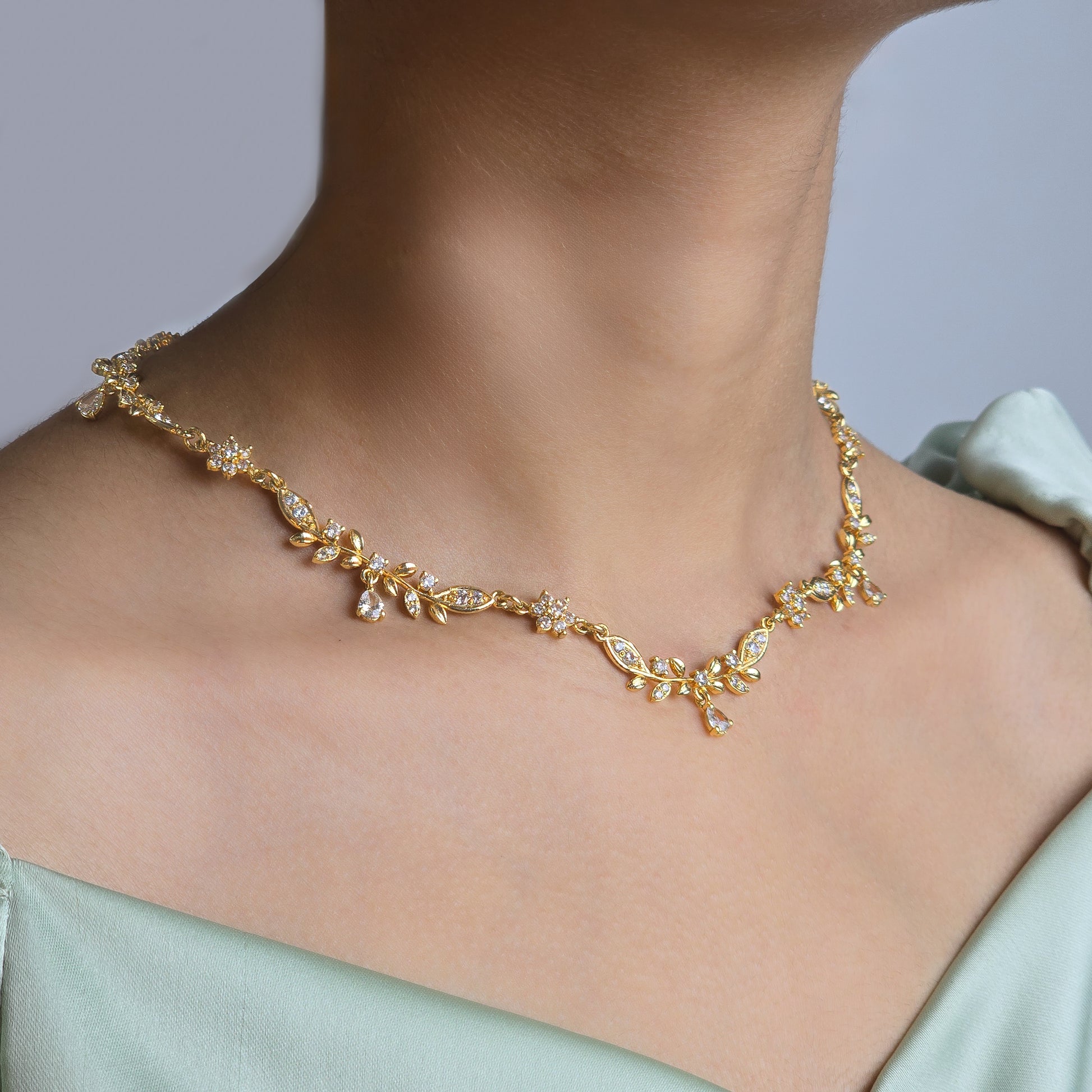 Gold necklace with leaf designs on a person wearing a light green top against a gray background