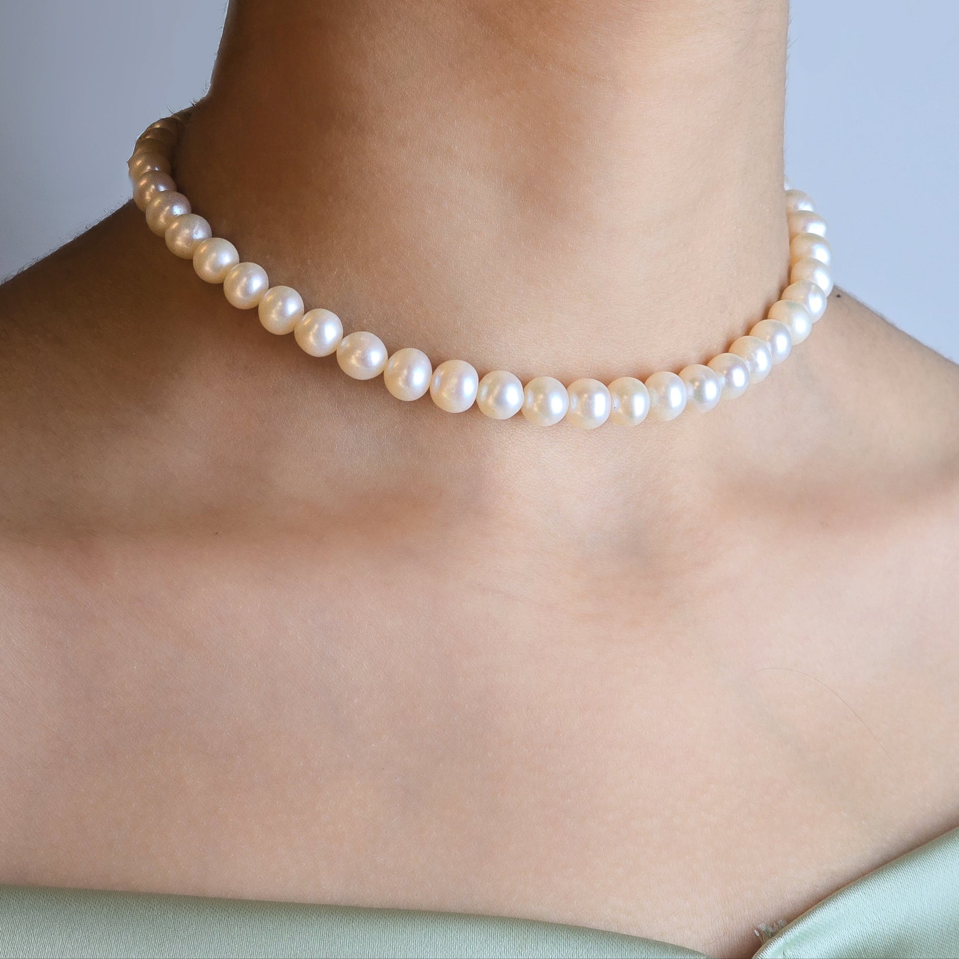 Pearl necklace worn by a person against a neutral background