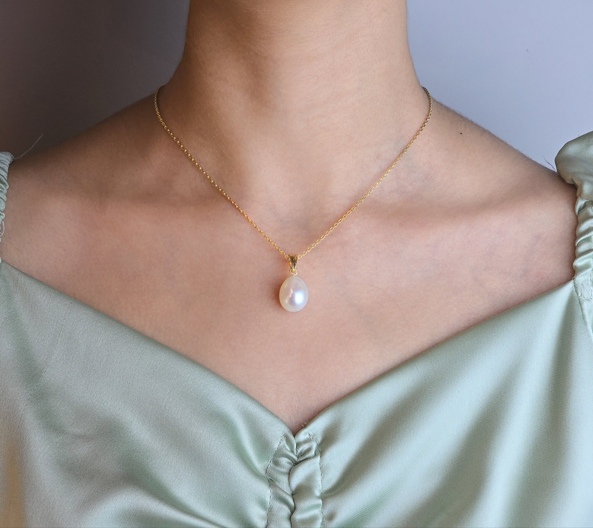 Pearl pendant on a gold chain against a white background