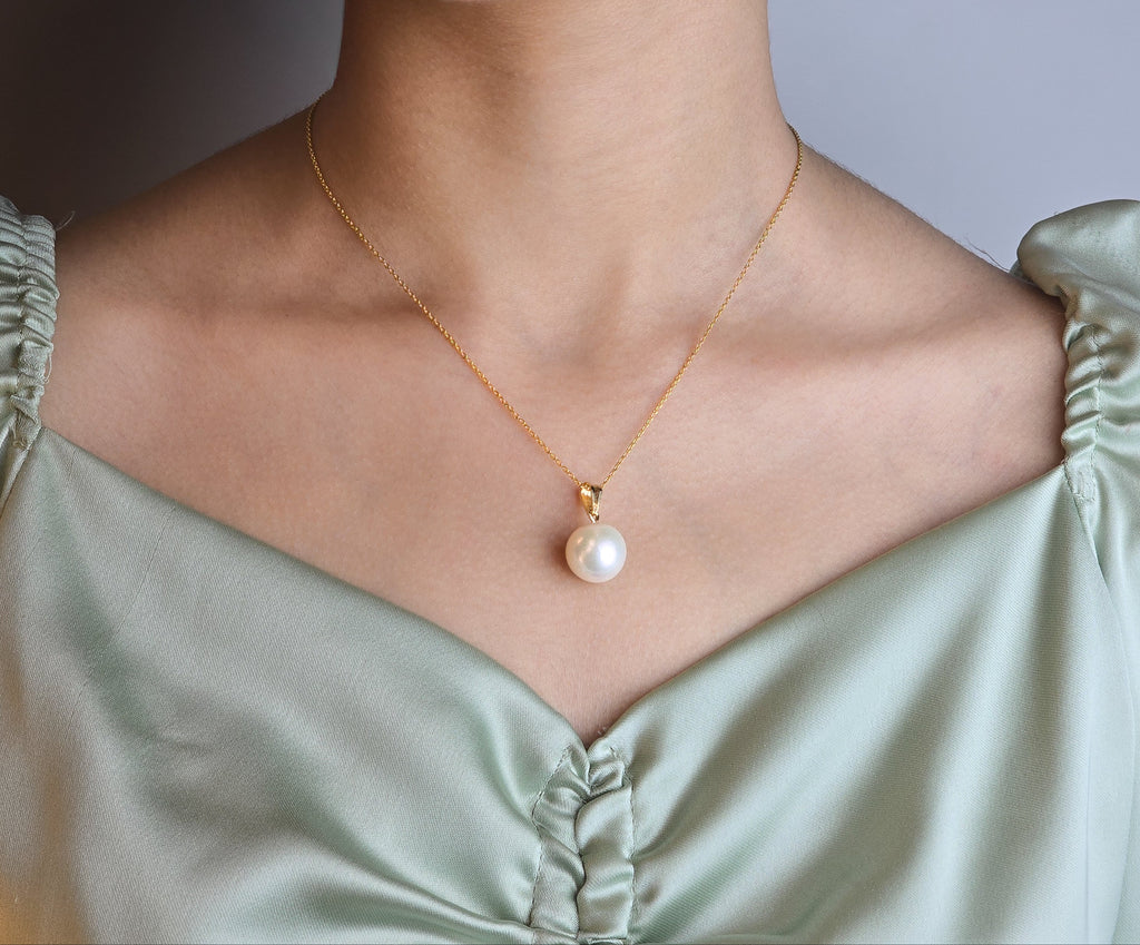 Pearl necklace on a person wearing a light green top against a neutral background