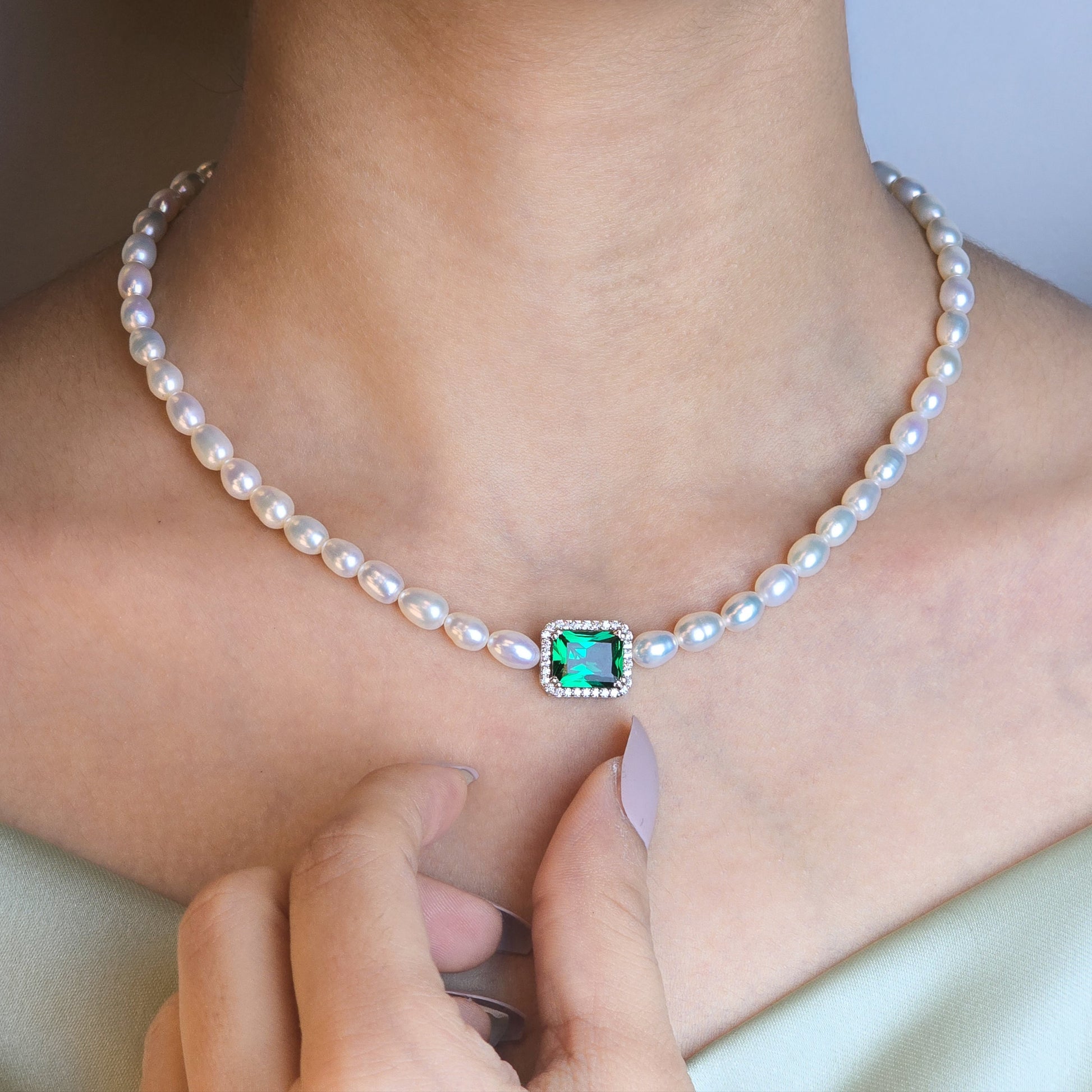 Pearl necklace with a green gemstone clasp worn by a person