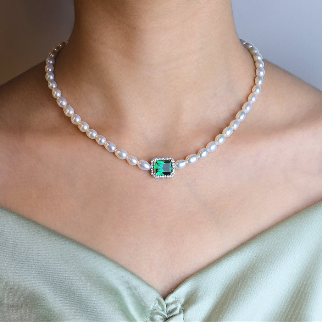 Pearl necklace with a green gemstone pendant on a person wearing a light green dress.