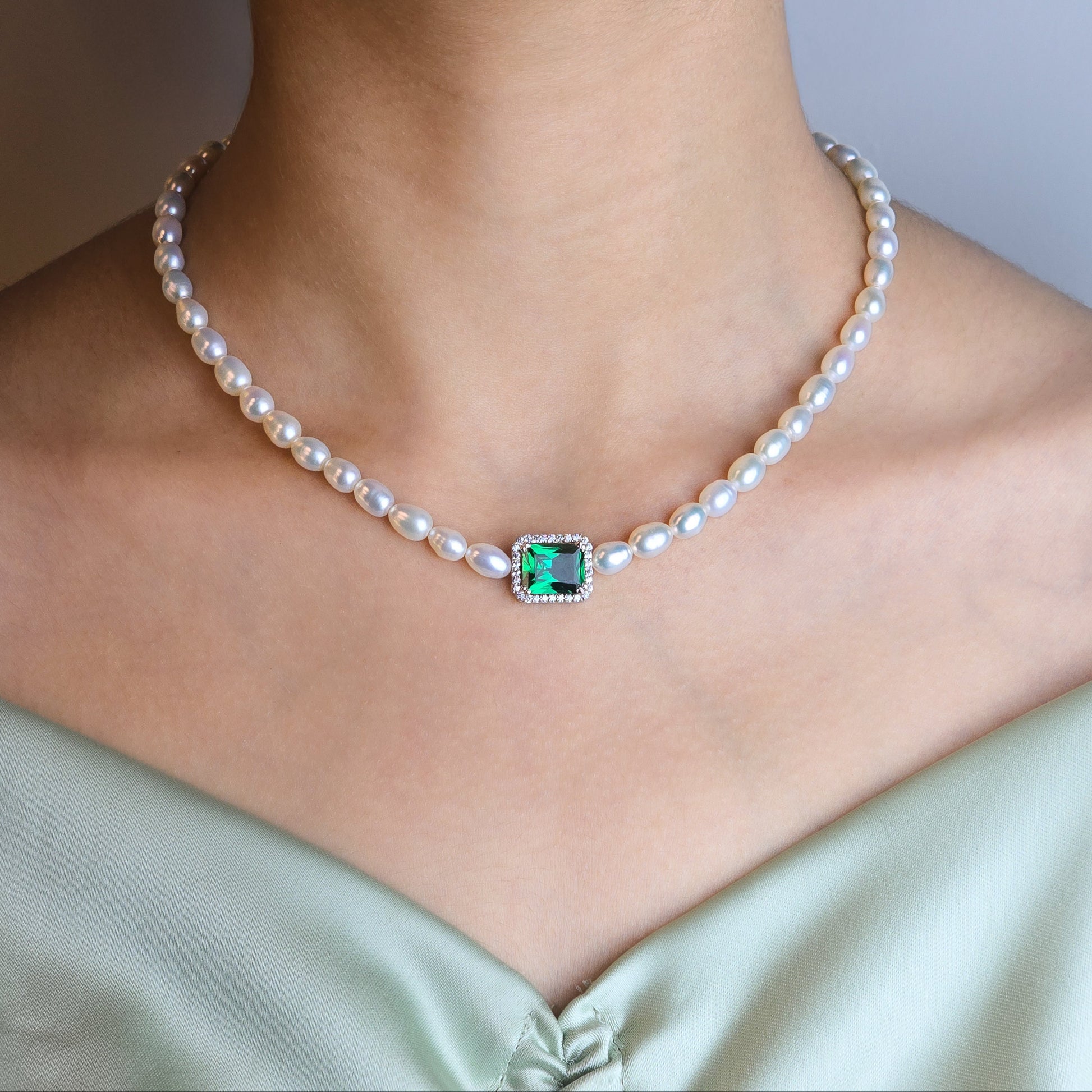 Pearl necklace with a green gemstone pendant on a person wearing a light green dress.