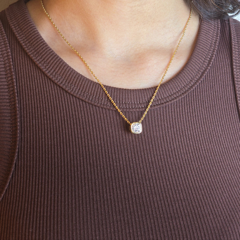 Gold necklace with a pendant worn by a person in a brown top.