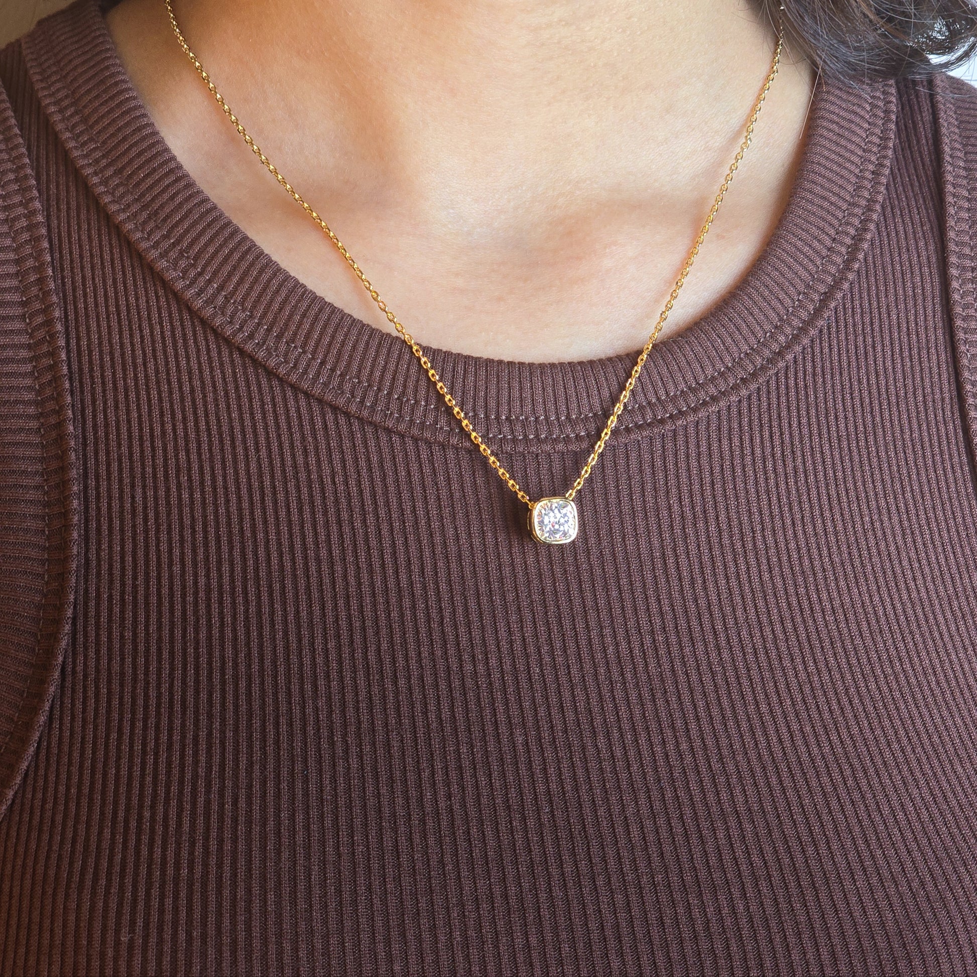 Gold necklace with a pendant worn by a person in a brown top.