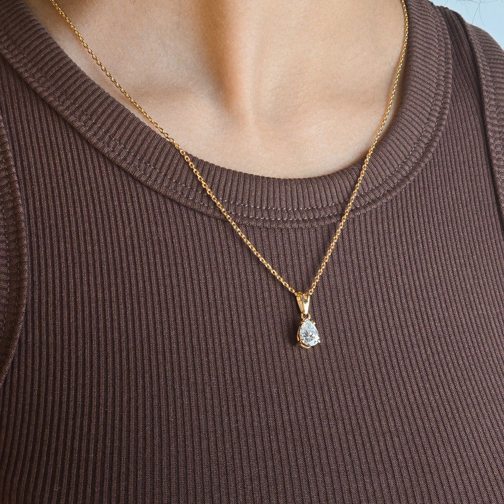 Person wearing a gold necklace with a pendant against a blue background