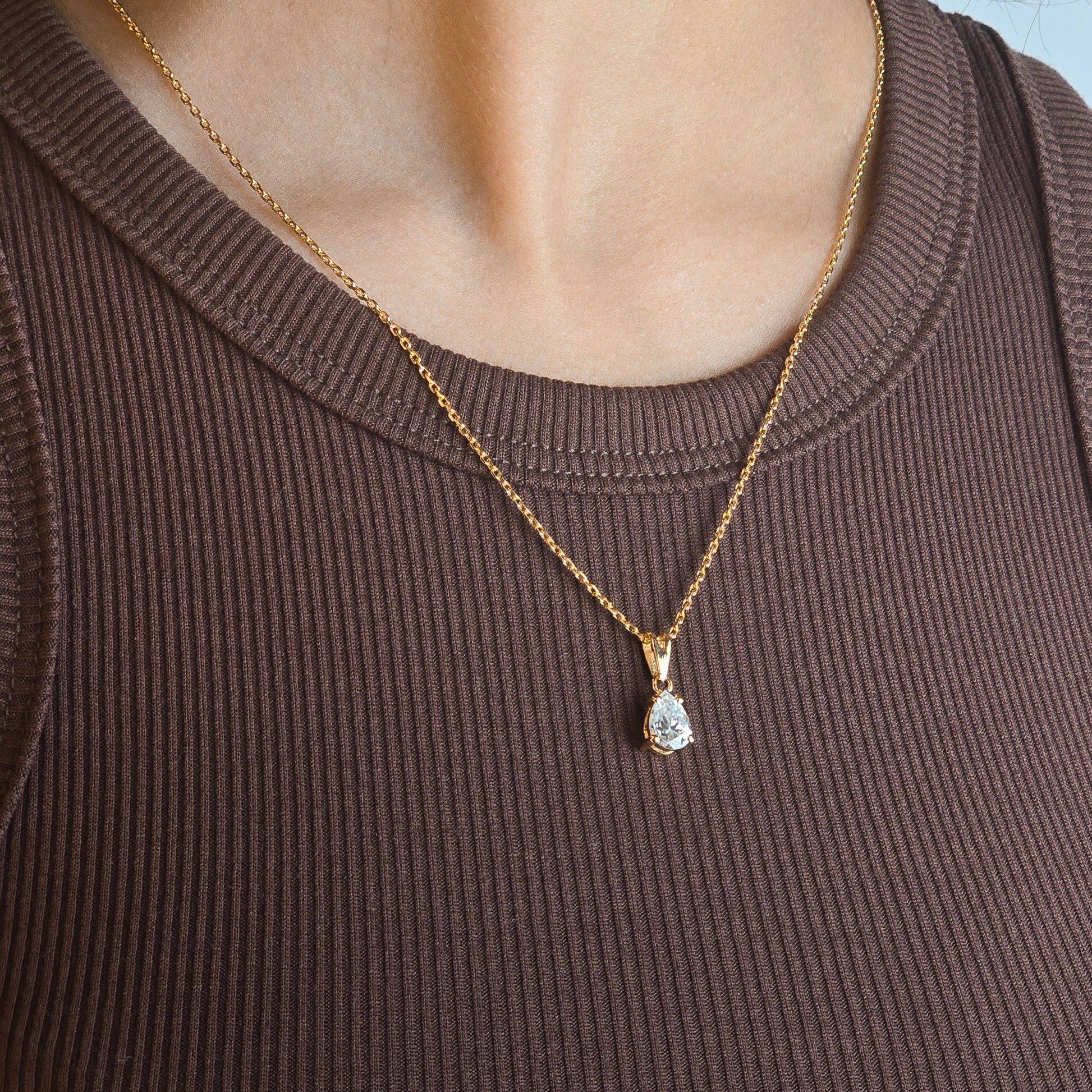 Person wearing a gold necklace with a pendant against a blue background