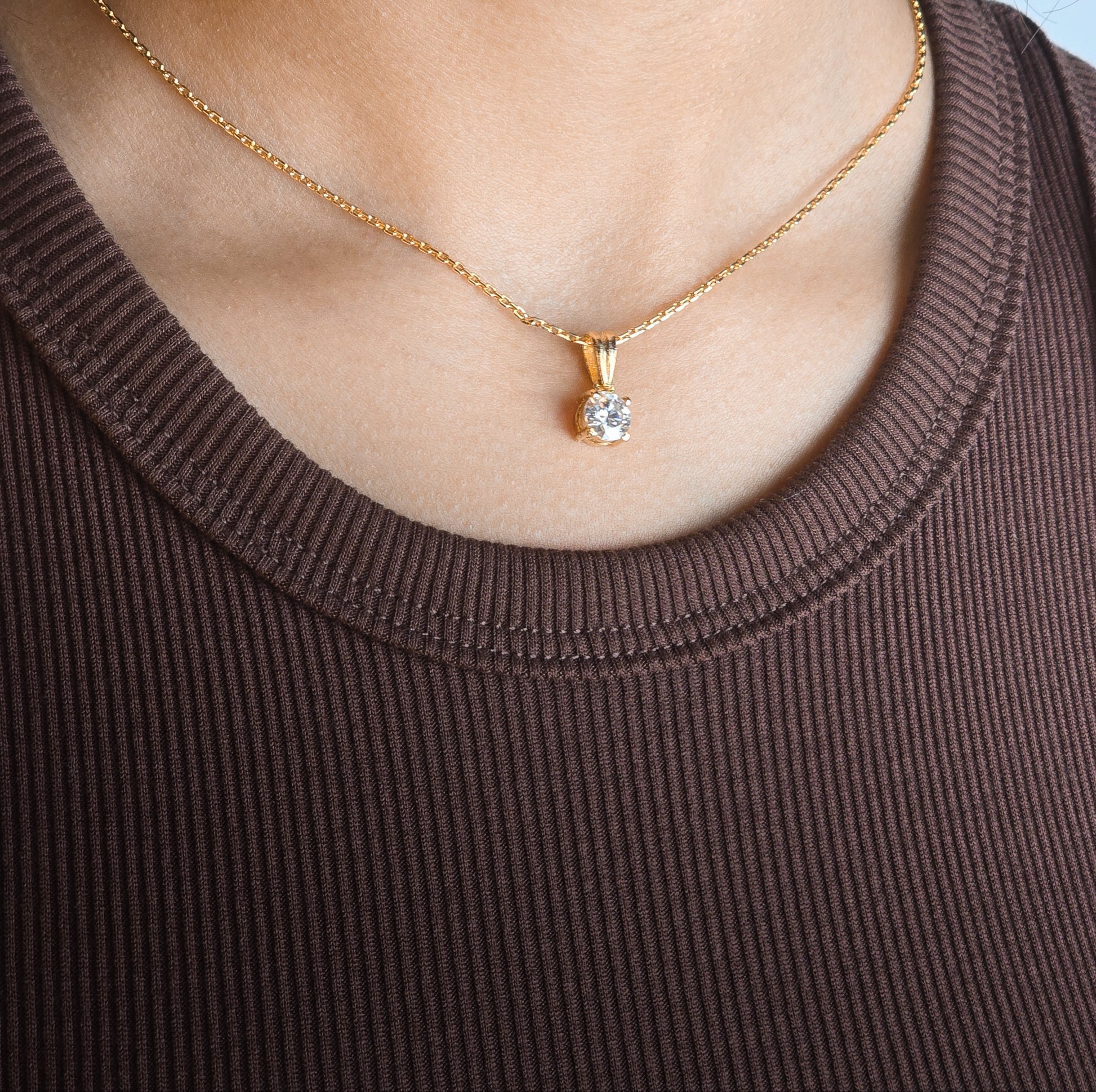 Gold necklace with a diamond pendant worn by a person in a brown top.