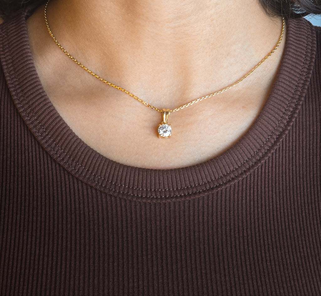 Gold necklace with a diamond pendant worn by a person in a brown top.