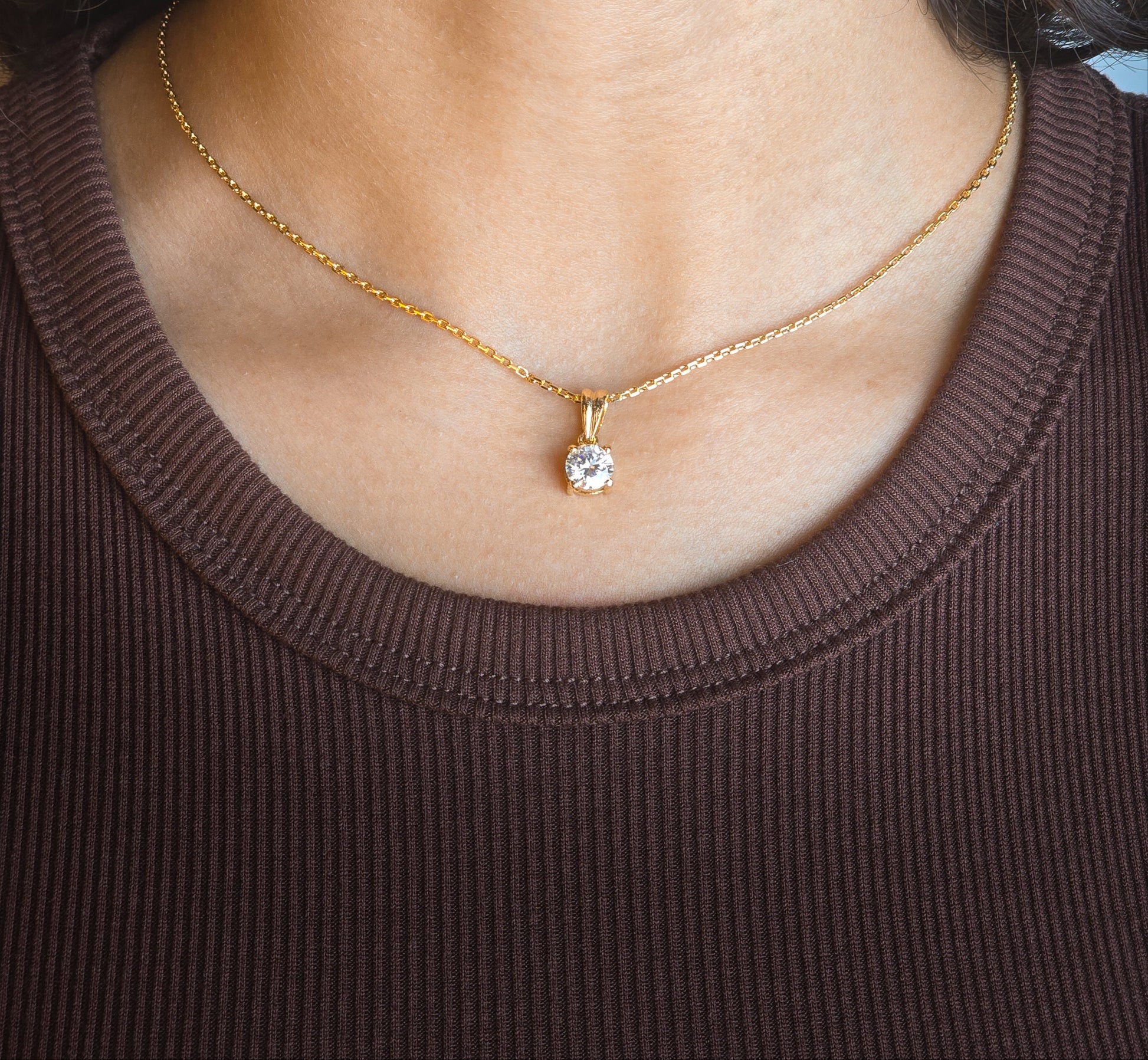 Gold necklace with a diamond pendant worn by a person in a brown top.