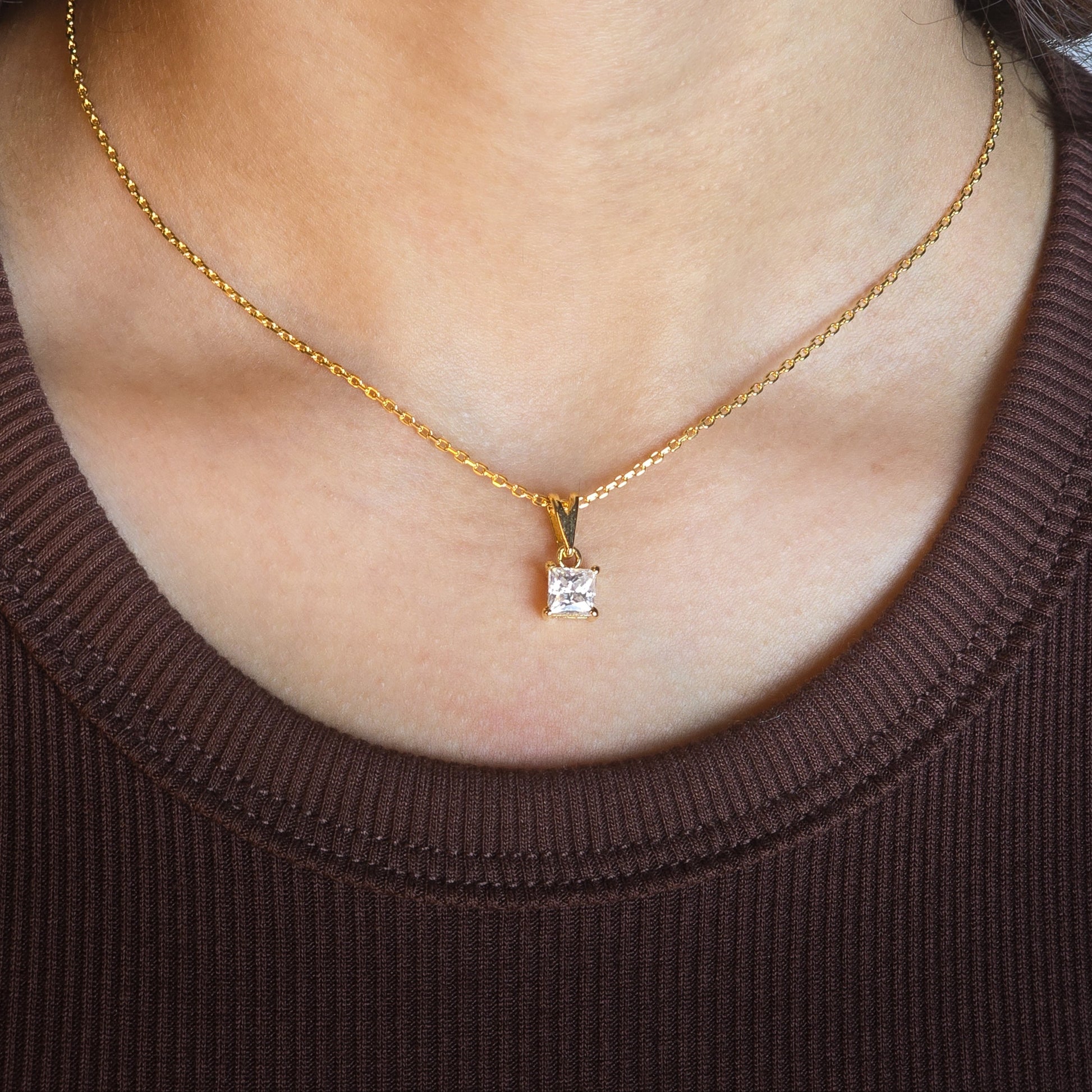 Gold necklace with a diamond pendant worn by a person in a brown sweater.