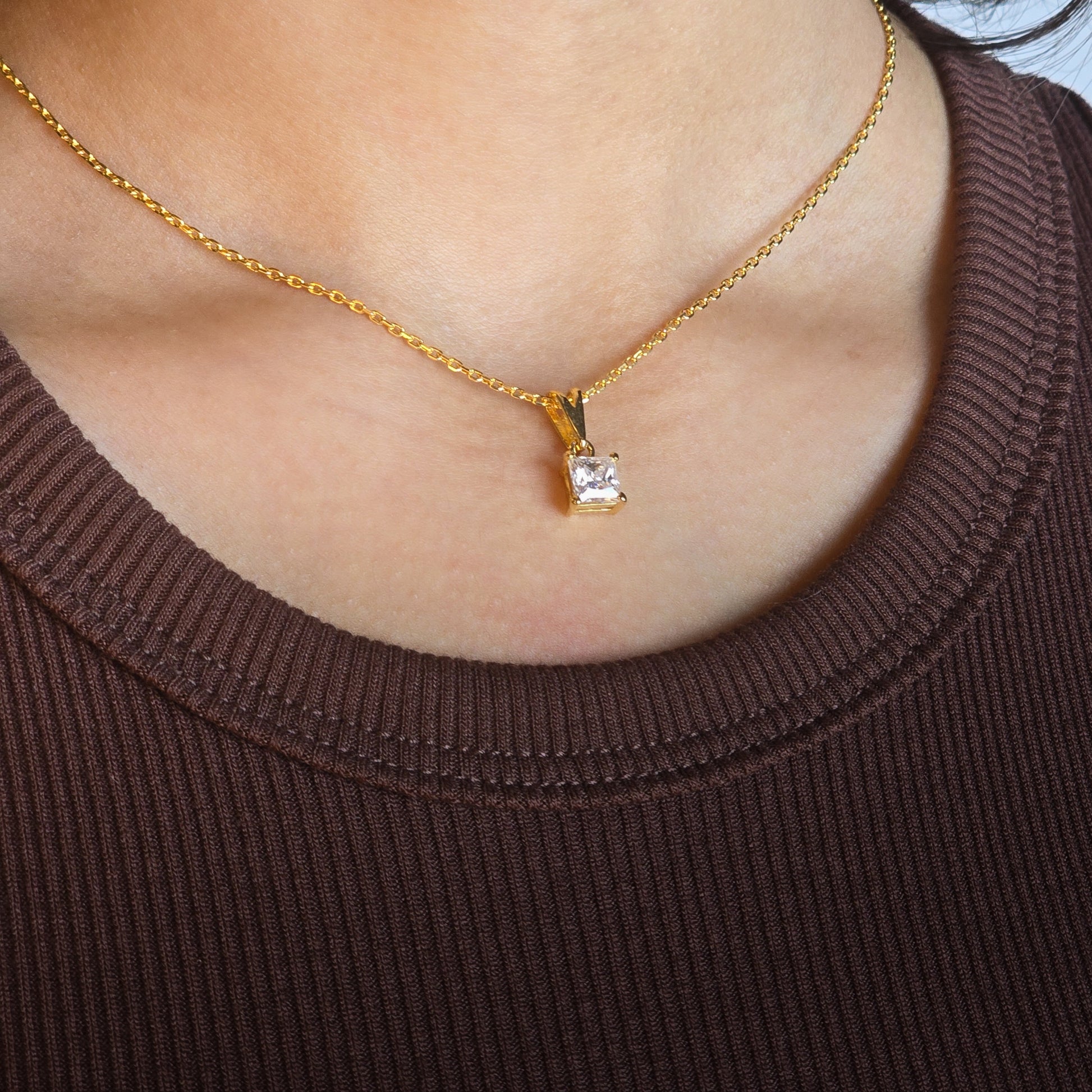 Gold necklace with a diamond pendant worn by a person in a brown top.