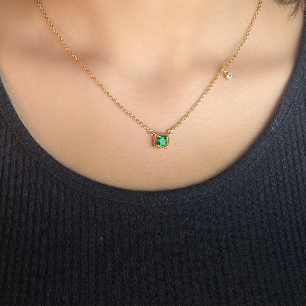 Gold necklace with a green gemstone pendant worn by a person in a black top.