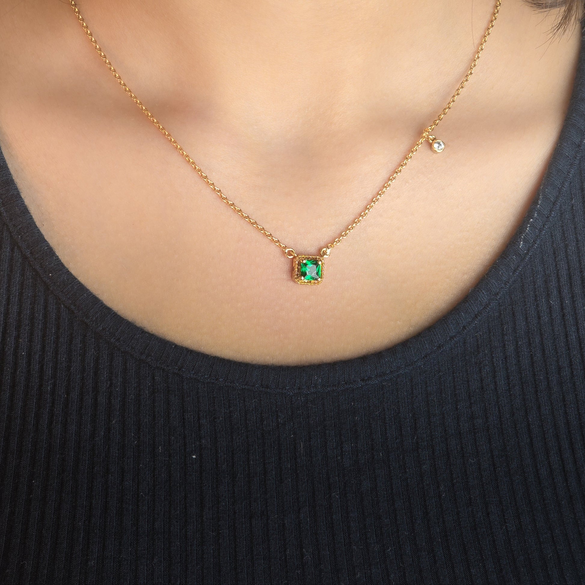 Gold necklace with a green gemstone pendant worn by a person in a black top.
