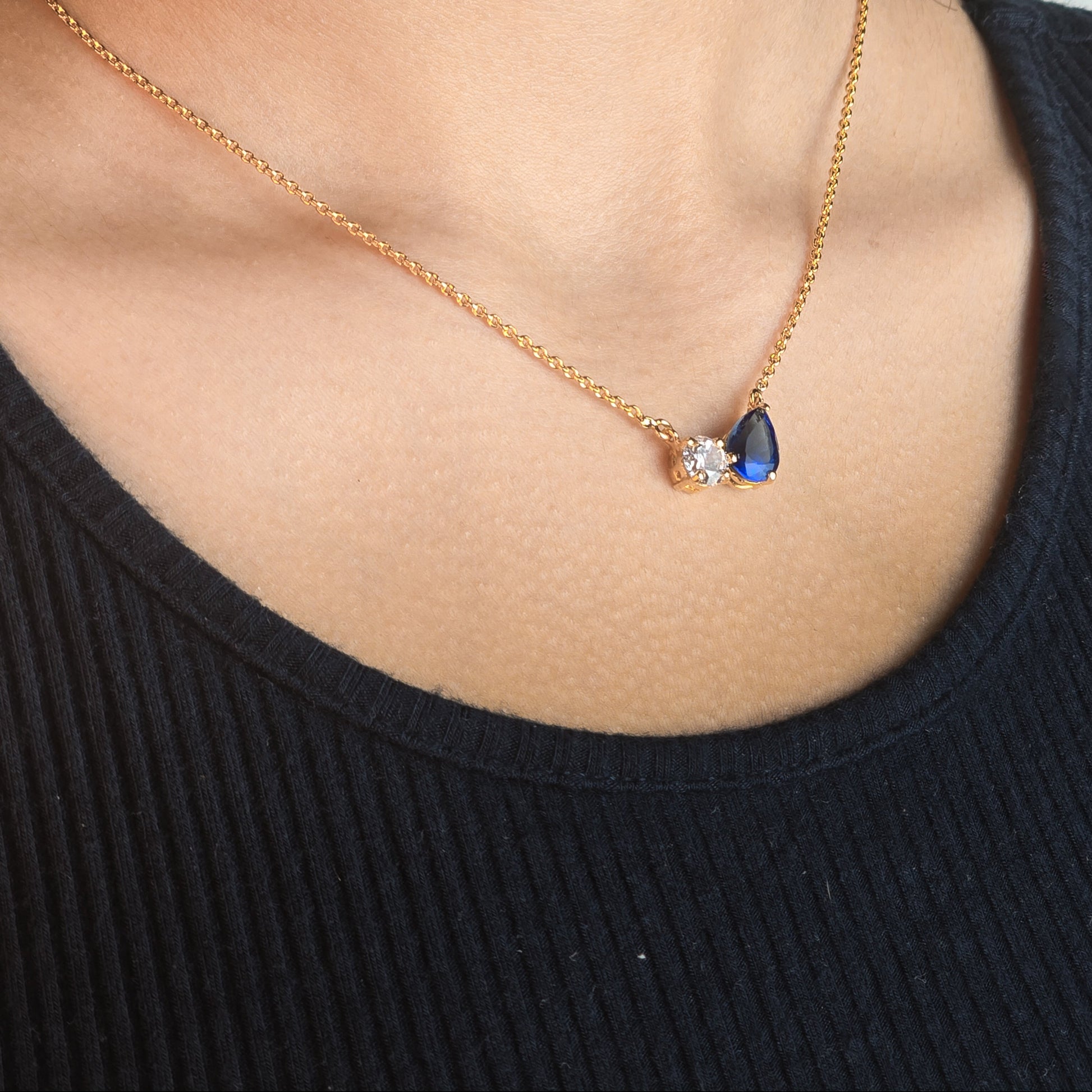 Necklace with a teardrop-shaped pendant featuring a blue gemstone worn by a person in a black top.