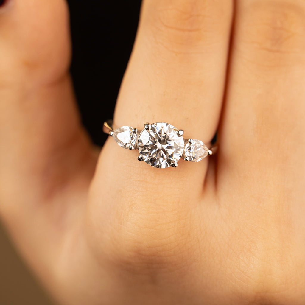 Mira ring worn on hand — round centre stone flanked by two pear side stones