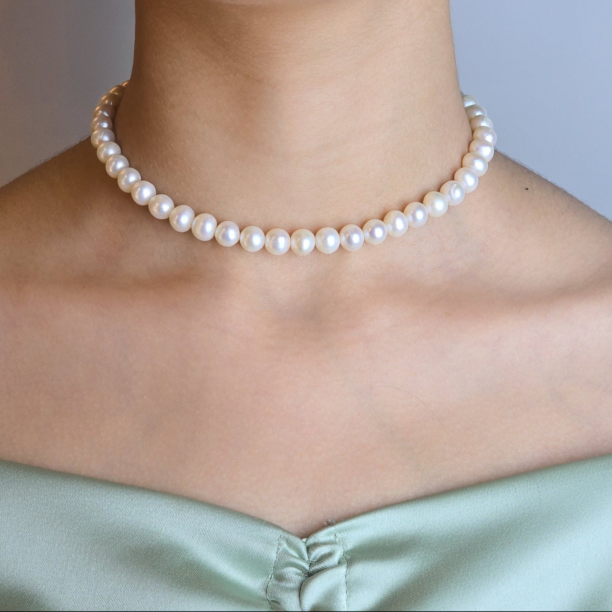 Pearl necklace worn by a person with a neutral background