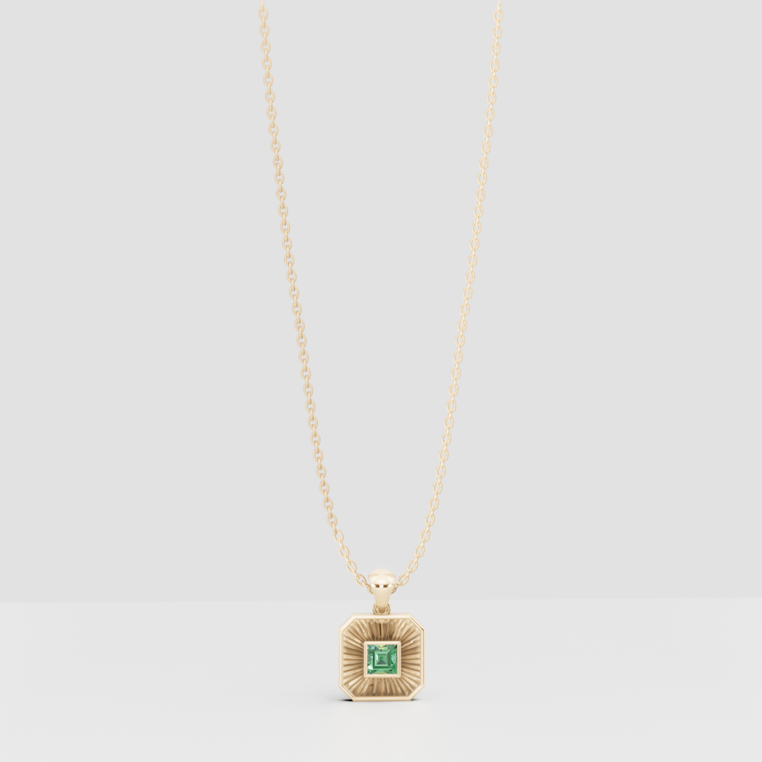 Gold necklace with a square pendant featuring a green gemstone on a light gray background